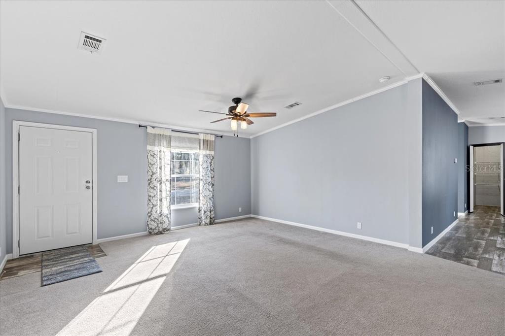 A living room with light gray walls, carpeted flooring, a ceiling fan, and a front door — 1910 NE 155TH COURT, WILLISTON, FL