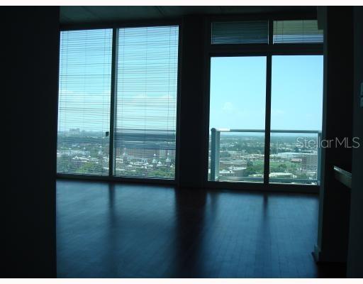 A room with dark hardwood floors and floor-to-ceiling windows overlooking a city skyline — 777 N ASHLEY DRIVE UNIT 1701, TAMPA, FL