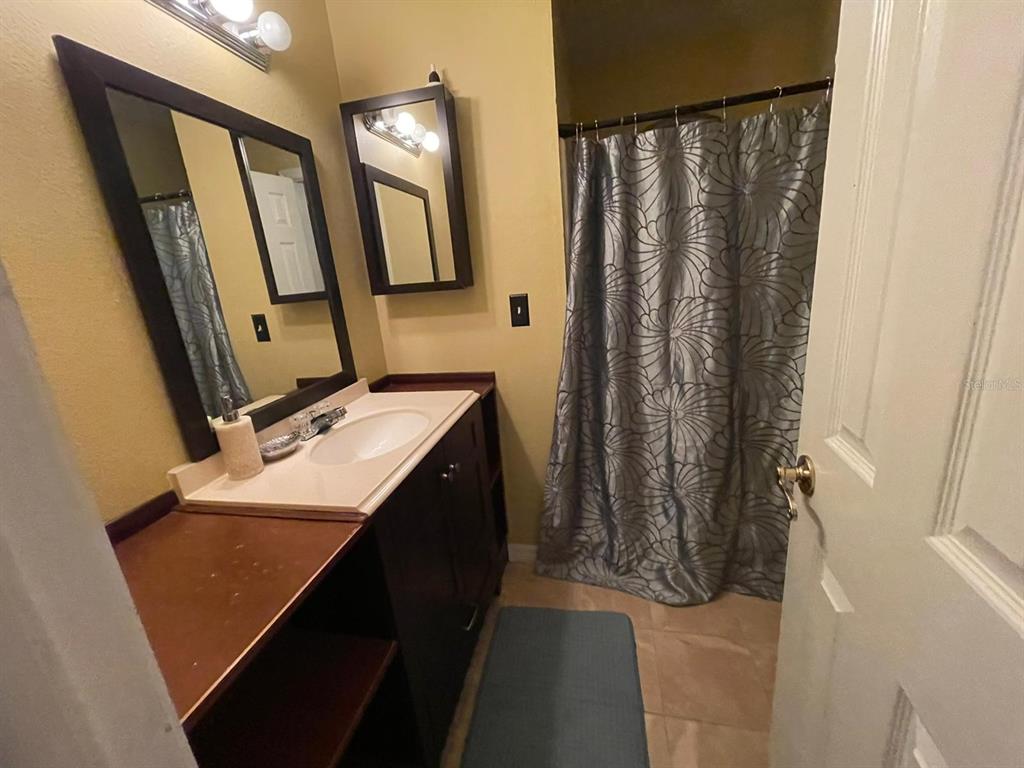 A bathroom features a dark wood vanity, a large mirror, and a patterned shower curtain — 2456 SWEETWATER CLUB CIRCLE UNIT 20, KISSIMMEE, FL