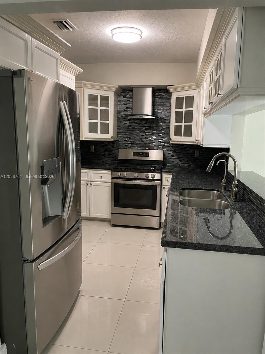 A kitchen features white cabinets, stainless steel appliances, dark granite countertops, and a tiled backsplash — 6129 SW 28th St, Miami FL 33155, MIAMI, FL