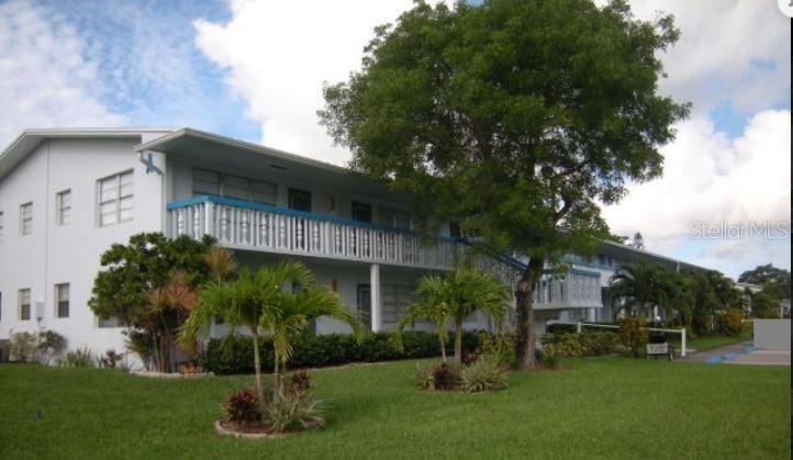 A two-story apartment building with a white exterior, blue railings, and a large front tree — 19 NEWPORT A, DEERFIELD BEACH, FL