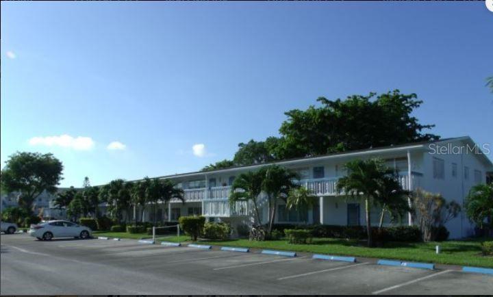 A two-story apartment building with a parking lot in the foreground and palm trees — 19 NEWPORT A, DEERFIELD BEACH, FL