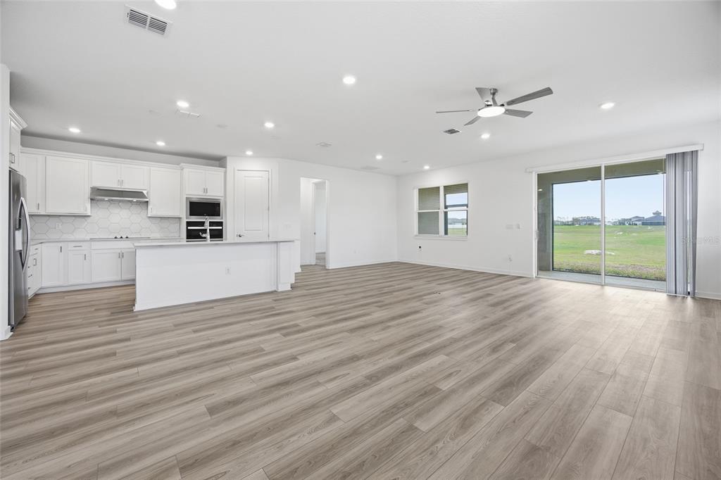 An open-concept kitchen and living area with white cabinets, light wood flooring, and sliding doors — 4311 SW 84TH STREET, OCALA, FL