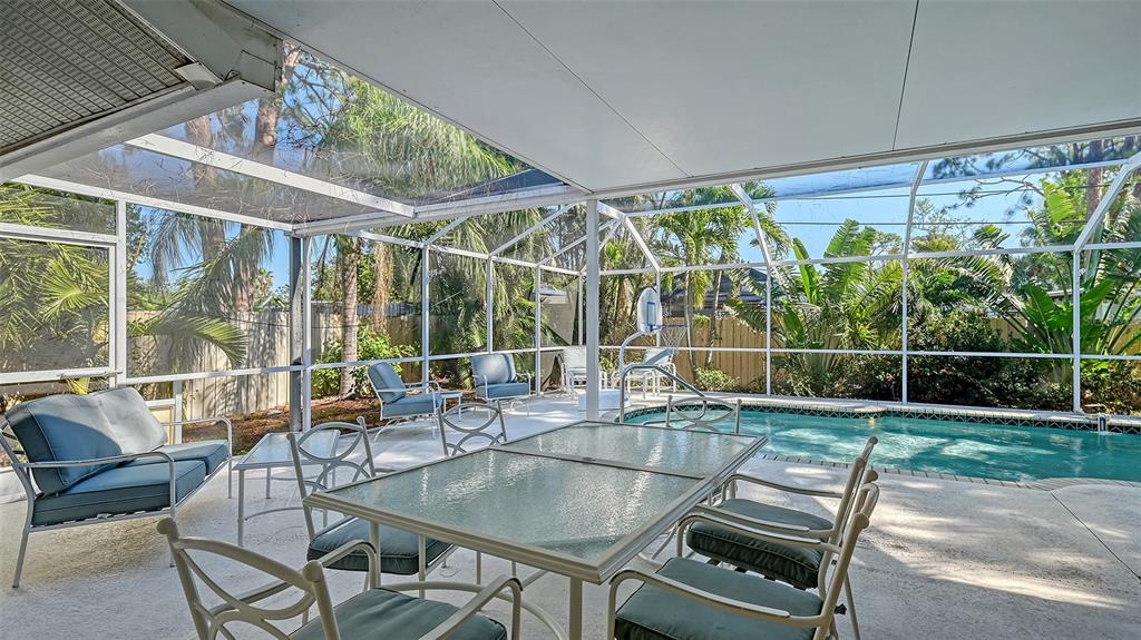 A covered patio with a dining set and lounge chairs overlooks a screened-in swimming pool — 5753 NEW YORK AVENUE, SARASOTA, FL