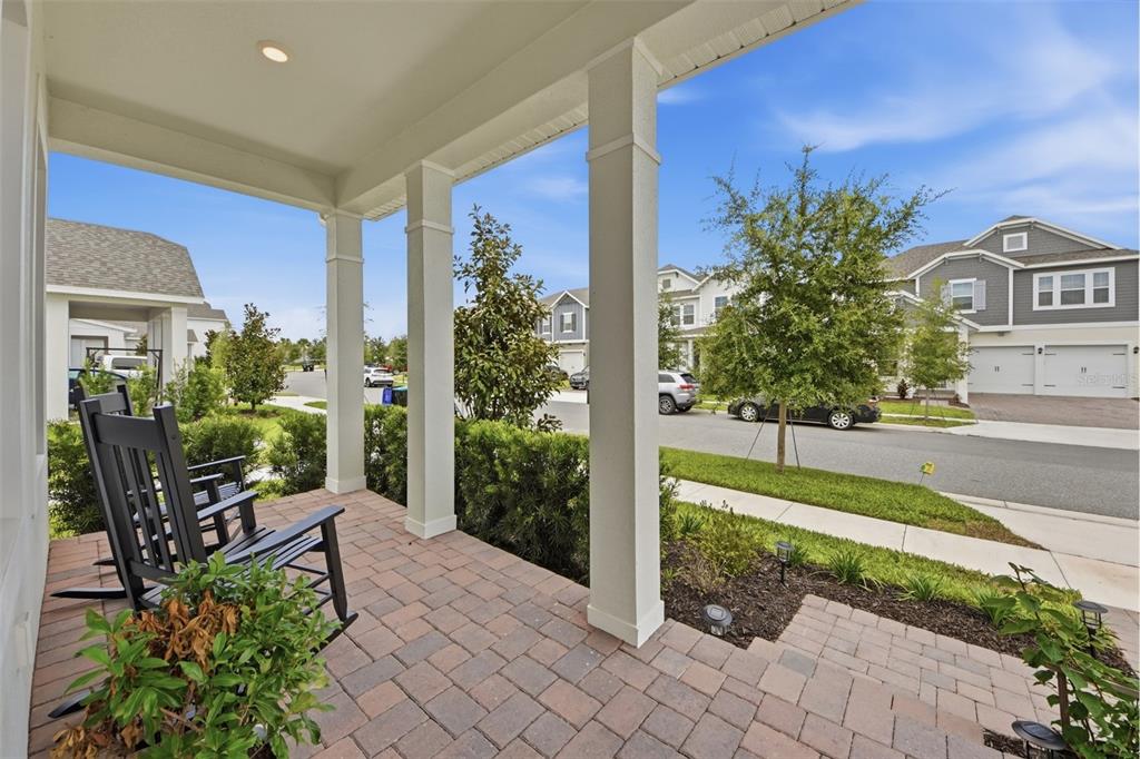 A covered brick porch with a rocking chair overlooks a suburban street and neighboring houses — 13061 SUNRISE HARVEST DRIVE, WINTER GARDEN, FL