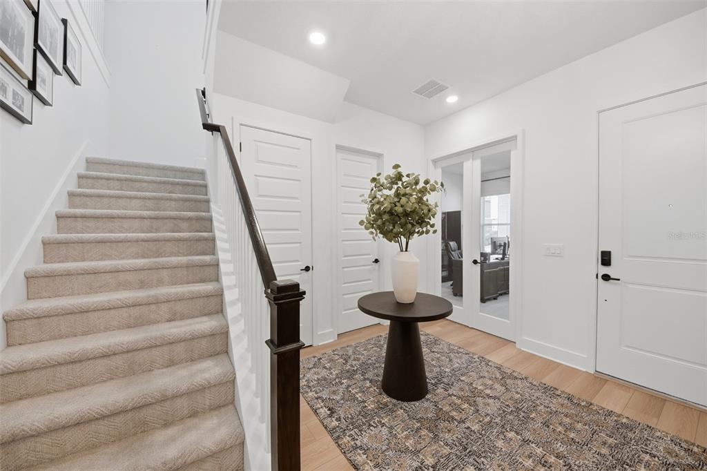 A bright entryway features a carpeted staircase, a round pedestal table, and glass-paneled double doors — 13061 SUNRISE HARVEST DRIVE, WINTER GARDEN, FL