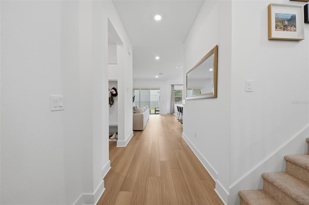 A bright hallway with light wood flooring leads toward an open living area and kitchen — 13061 SUNRISE HARVEST DRIVE, WINTER GARDEN, FL