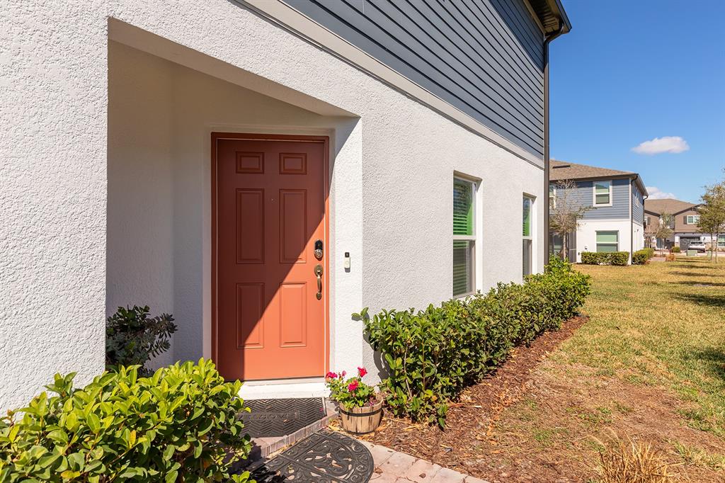 A red front door is set into a white stucco exterior wall with green bushes — 170 CAPE HONEYSUCKLE PLACE, SANFORD, FL