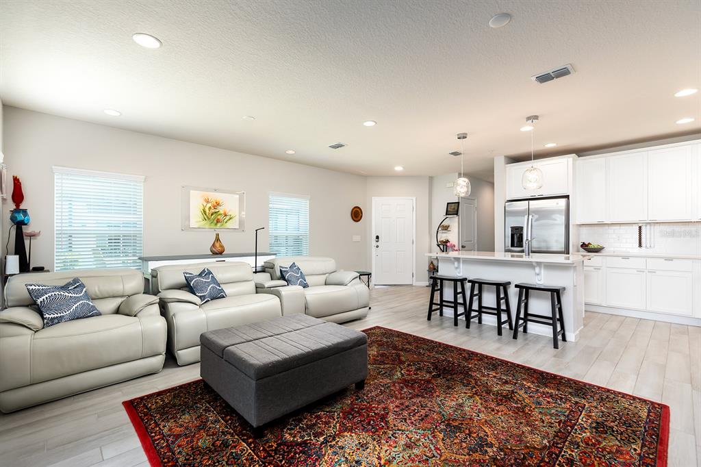 An open-concept living room and kitchen featuring light flooring, white cabinetry, and a patterned rug — 170 CAPE HONEYSUCKLE PLACE, SANFORD, FL