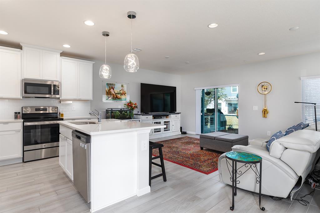 An open-concept kitchen and living area features white cabinetry, stainless appliances, and a red rug — 170 CAPE HONEYSUCKLE PLACE, SANFORD, FL