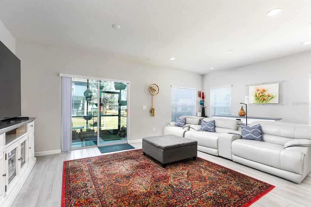 A living room features a white leather sofa, a patterned rug, and a sliding glass door — 170 CAPE HONEYSUCKLE PLACE, SANFORD, FL