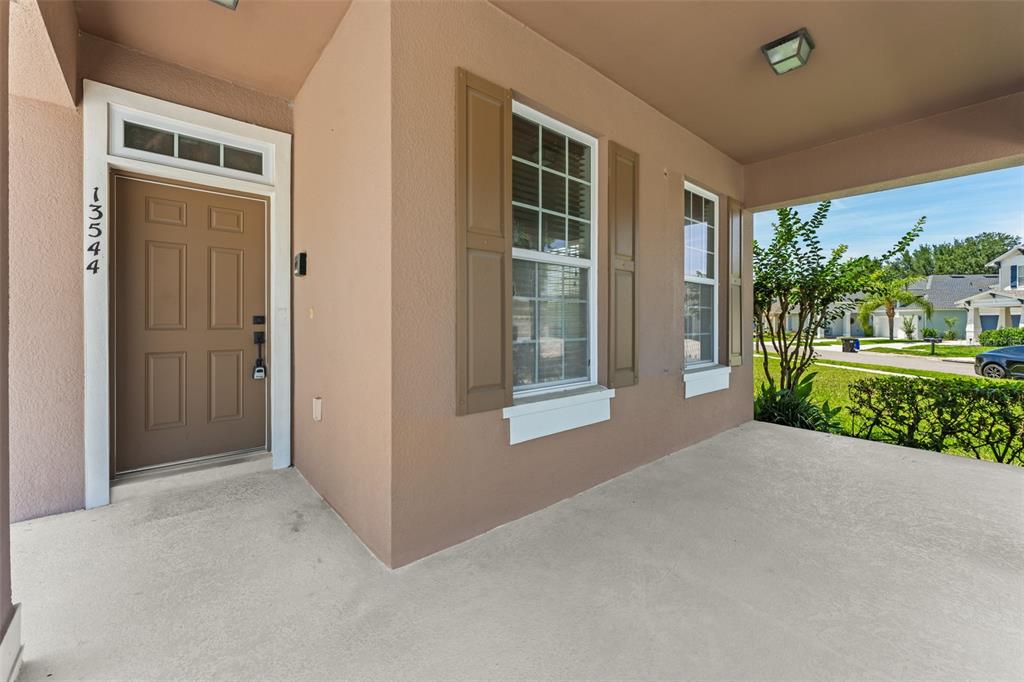 A covered front porch features a brown door, two windows with shutters, and concrete flooring — 13544 RIGGS WAY, WINDERMERE, FL