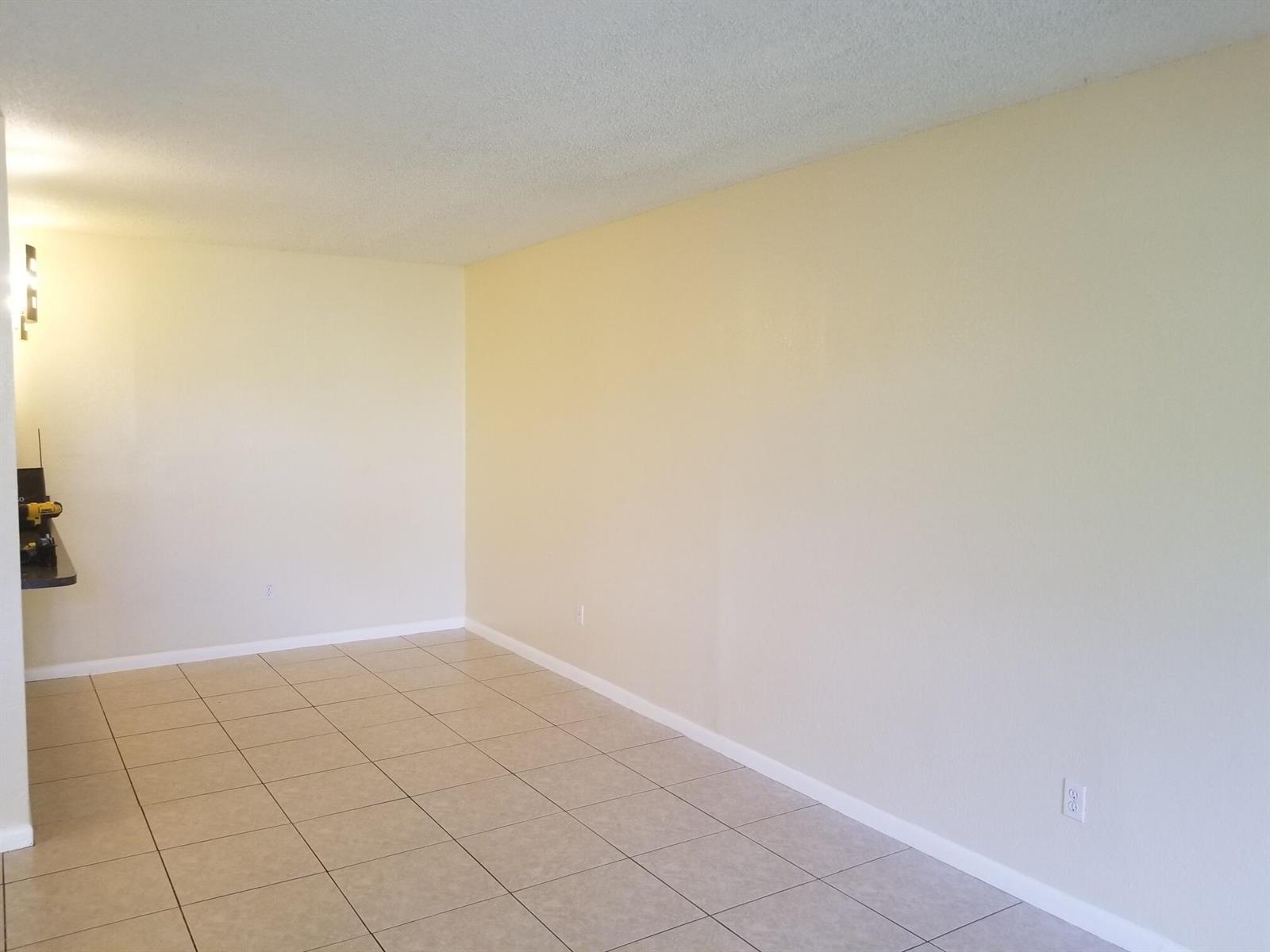 An empty room with light-colored walls, beige tile flooring, and a partial view of a counter — 6023 10th Avenue N # 114, FL 33463, FL