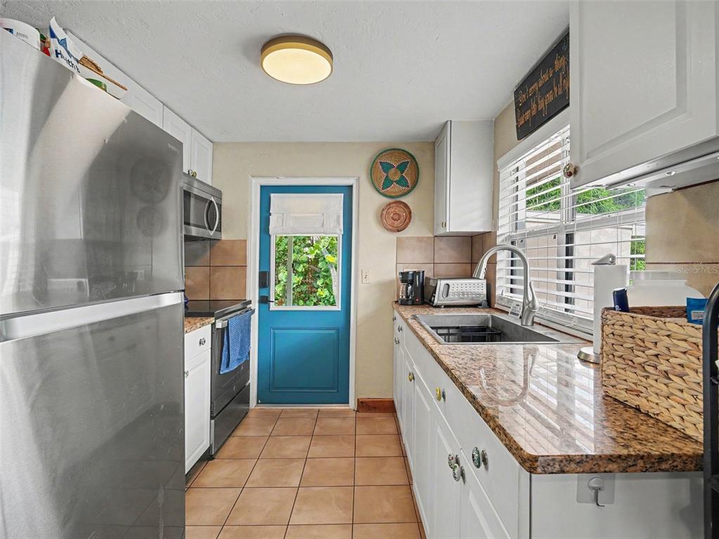 A galley kitchen features white cabinets, granite countertops, stainless steel appliances, and a blue door — 3035 HILLVIEW STREET, SARASOTA, FL
