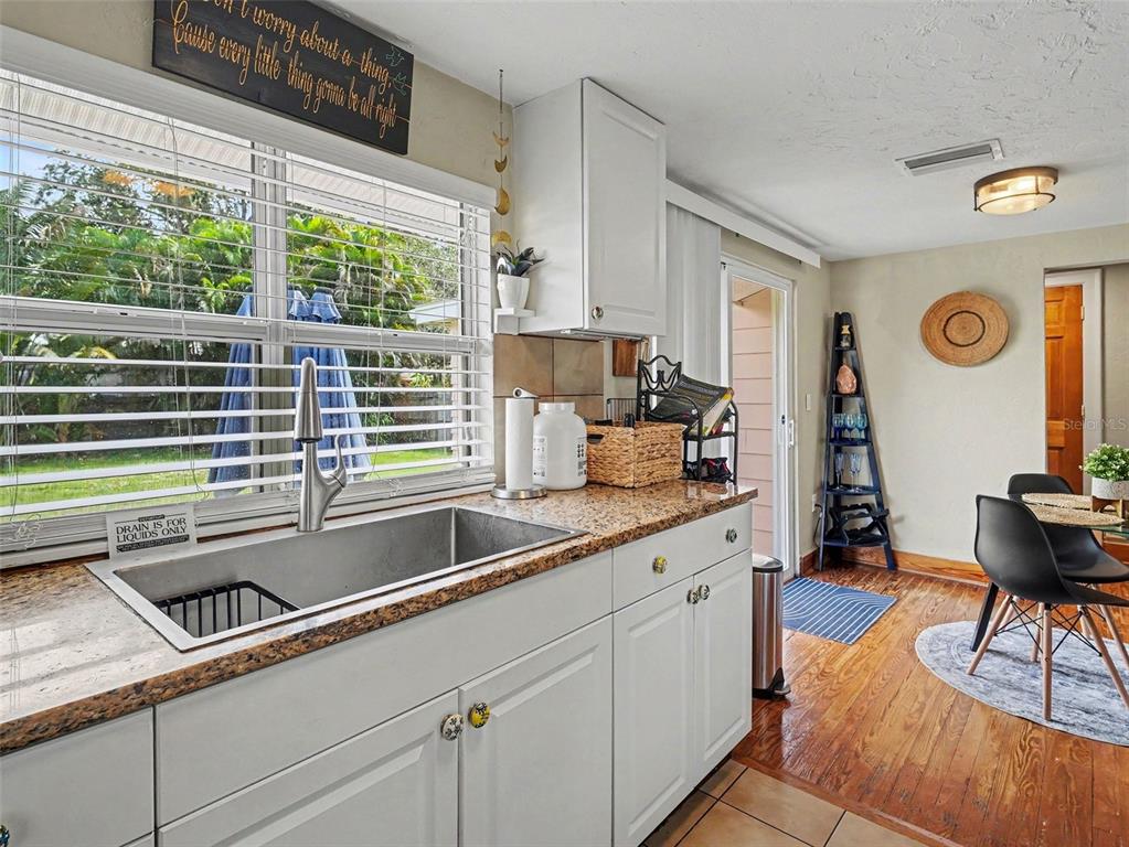 A kitchen with white cabinets, granite countertops, a stainless steel sink, and a dining area — 3035 HILLVIEW STREET, SARASOTA, FL