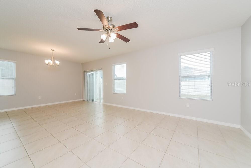 An empty living room features light tile flooring, a ceiling fan, and sliding glass doors — 1883 GREEN DRAGON DRIVE, ST CLOUD, FL