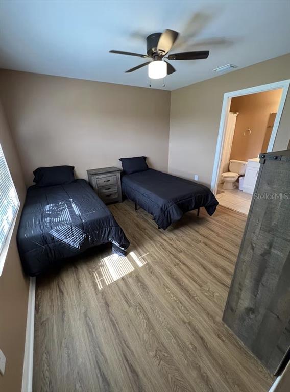 A bedroom with two twin beds, wood-look flooring, a ceiling fan, and an attached bathroom — 2211 SE 3RD STREET UNIT 1, BOYNTON BEACH, FL