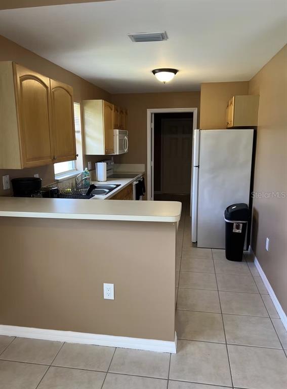 A kitchen with light wood cabinets, tan walls, tile flooring, and a breakfast bar — 2211 SE 3RD STREET UNIT 1, BOYNTON BEACH, FL