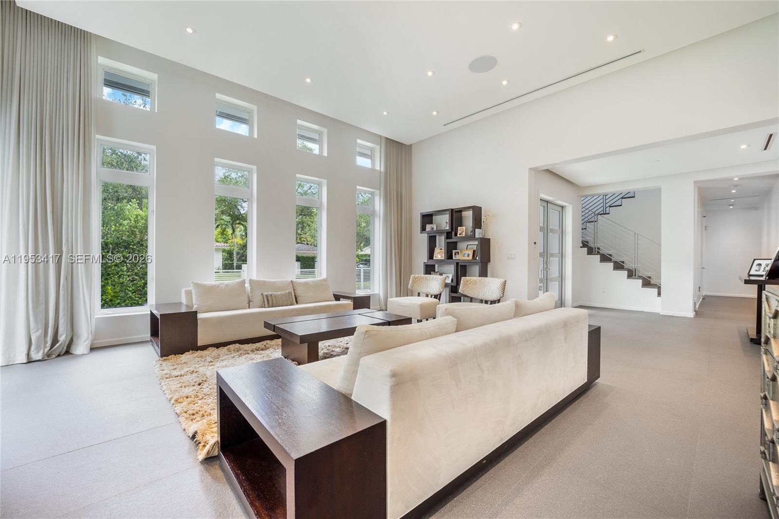 A bright living room features high ceilings, floor-to-ceiling windows, a fireplace, and neutral furniture — 6900 Barquera St, Coral Gables FL 33146, CORAL GABLES, FL