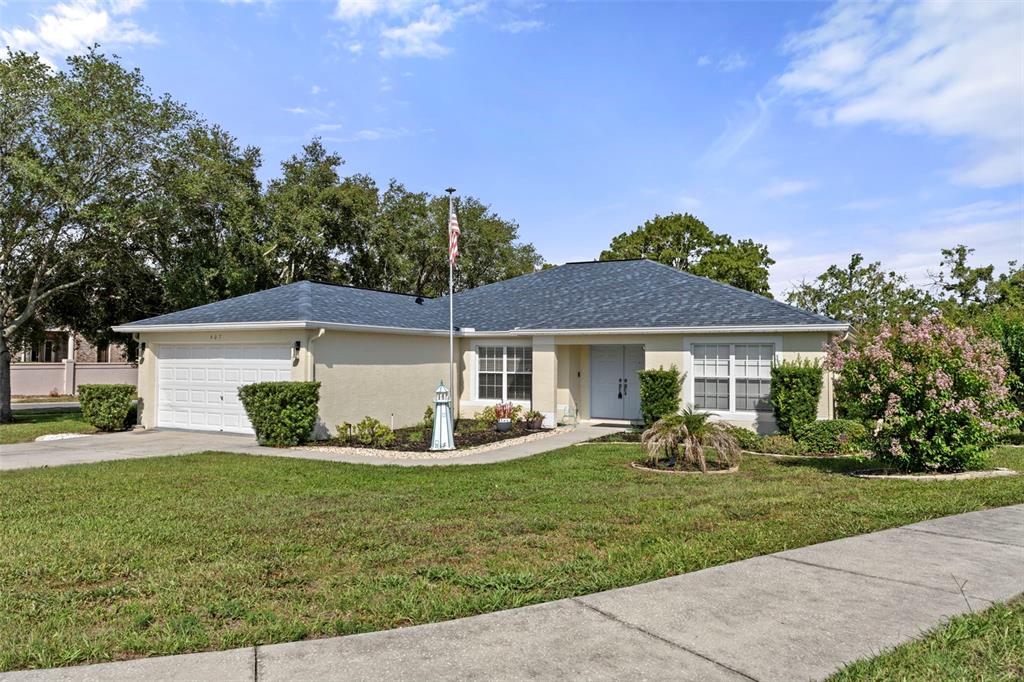 A single-story house with a white garage, light-colored stucco exterior, and a dark shingled roof — 407 MONTPELIER COURT, SPRING HILL, FL
