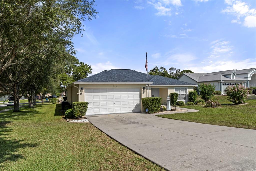 A single-story house with a two-car garage and a concrete driveway under a blue sky — 407 MONTPELIER COURT, SPRING HILL, FL