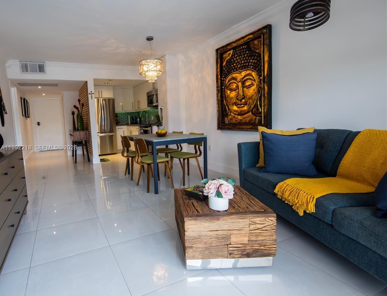 A living and dining area features a blue sofa, wooden coffee table, and Buddha wall art — 1650 NE 115th St # 302, Miami FL 33181, MIAMI, FL
