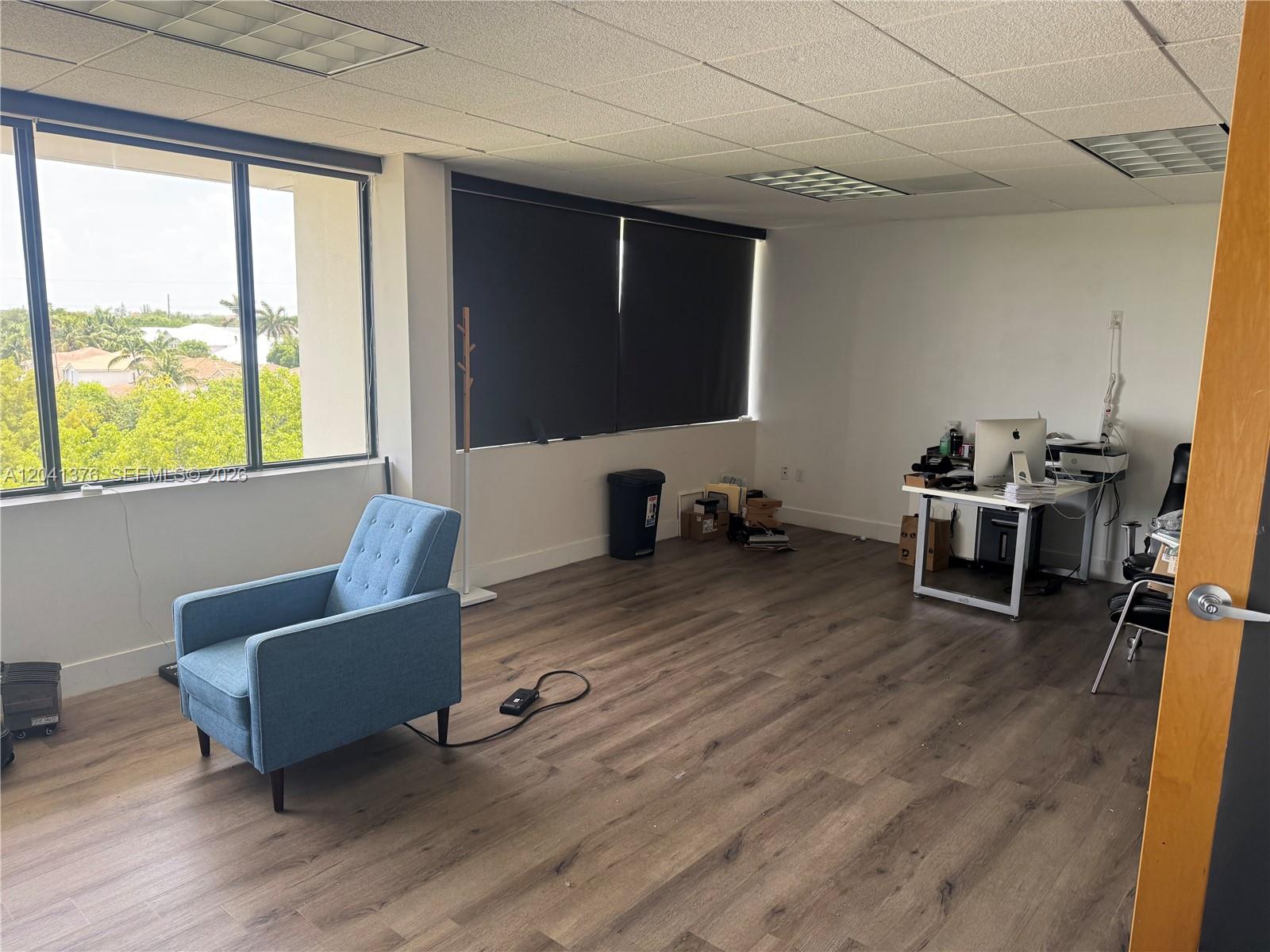 An office space features wood-look flooring, a blue armchair, a desk, and large windows — 8700 W Flagler St # 408, Miami FL 33174, MIAMI, FL