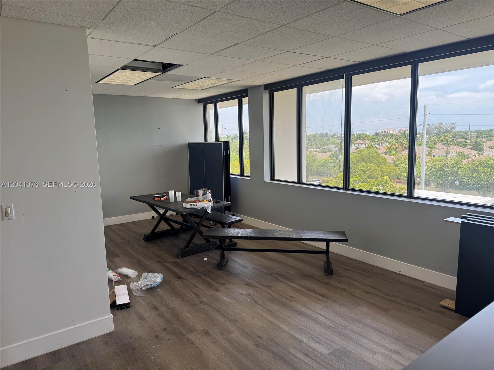 An office space features wood-look flooring, a table with benches, and large windows overlooking trees — 8700 W Flagler St # 408, Miami FL 33174, MIAMI, FL