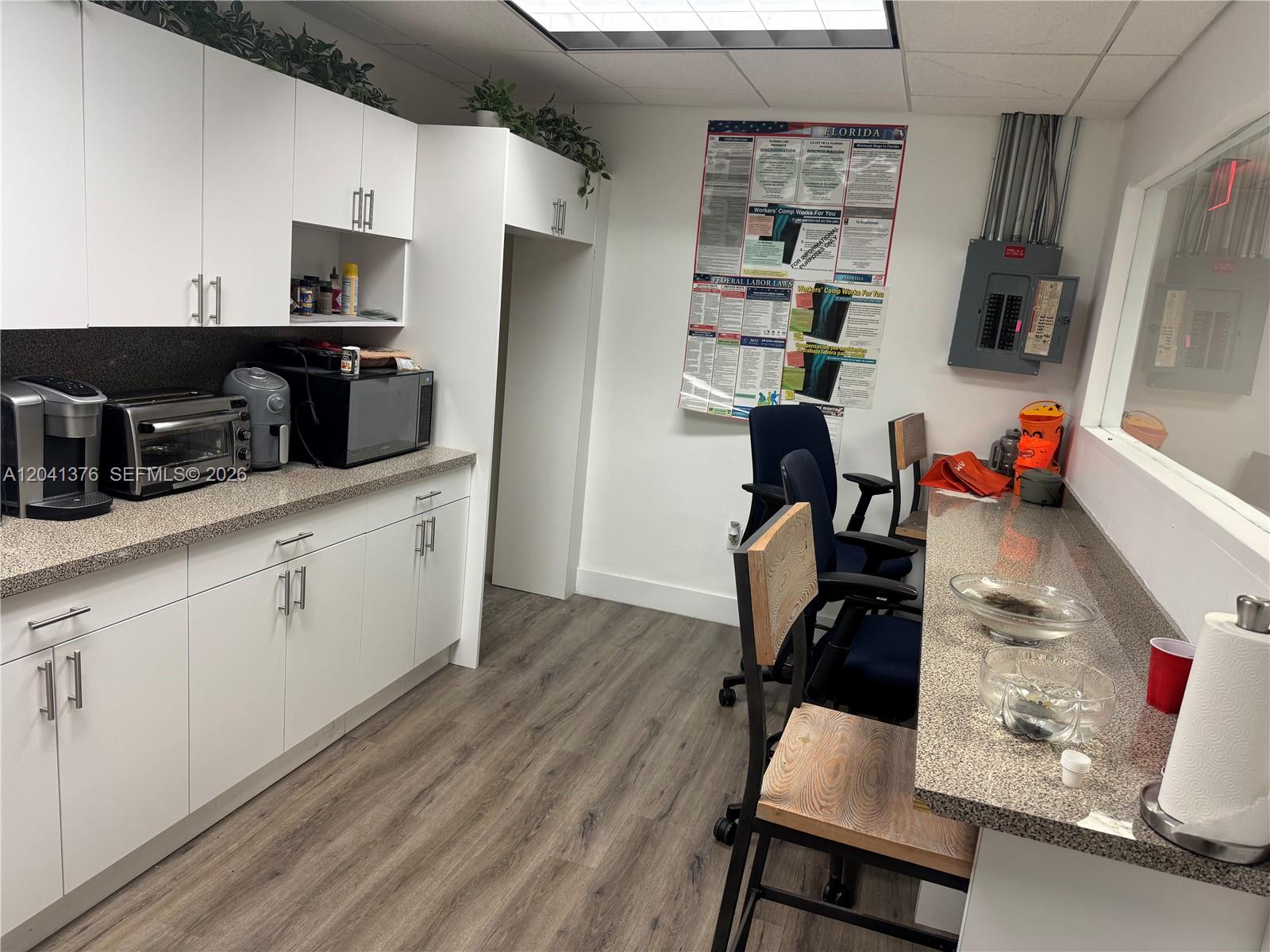 A breakroom features white cabinetry, granite countertops, wood-look flooring, and a wall-mounted electrical panel — 8700 W Flagler St # 408, Miami FL 33174, MIAMI, FL