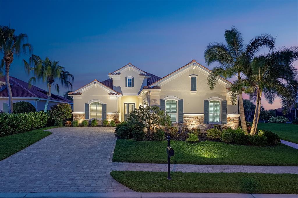 A single-story house with a paved driveway, stone accents, and palm trees at dusk — 1744 GRANDE PARK DRIVE, ENGLEWOOD, FL