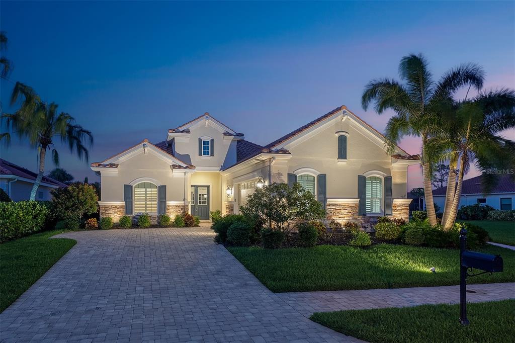 A single-story house with a stone facade, paved driveway, and palm trees at dusk — 1744 GRANDE PARK DRIVE, ENGLEWOOD, FL