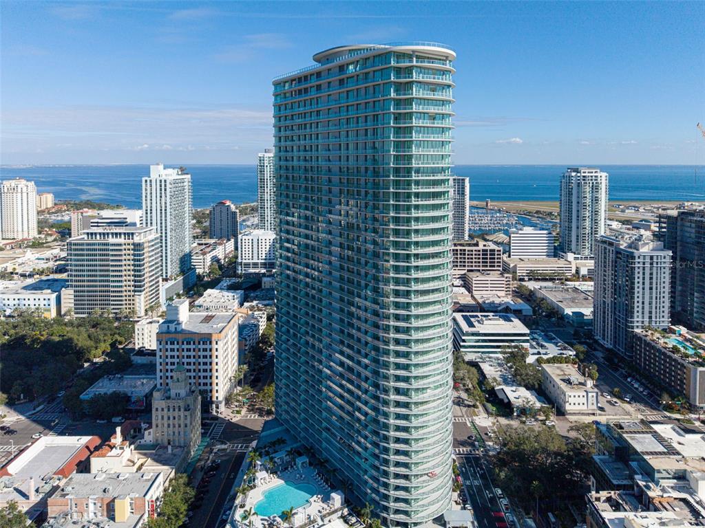 An aerial view of a tall, curved glass skyscraper surrounded by a dense urban cityscape — 400 CENTRAL AVENUE UNIT 3603, ST PETERSBURG, FL