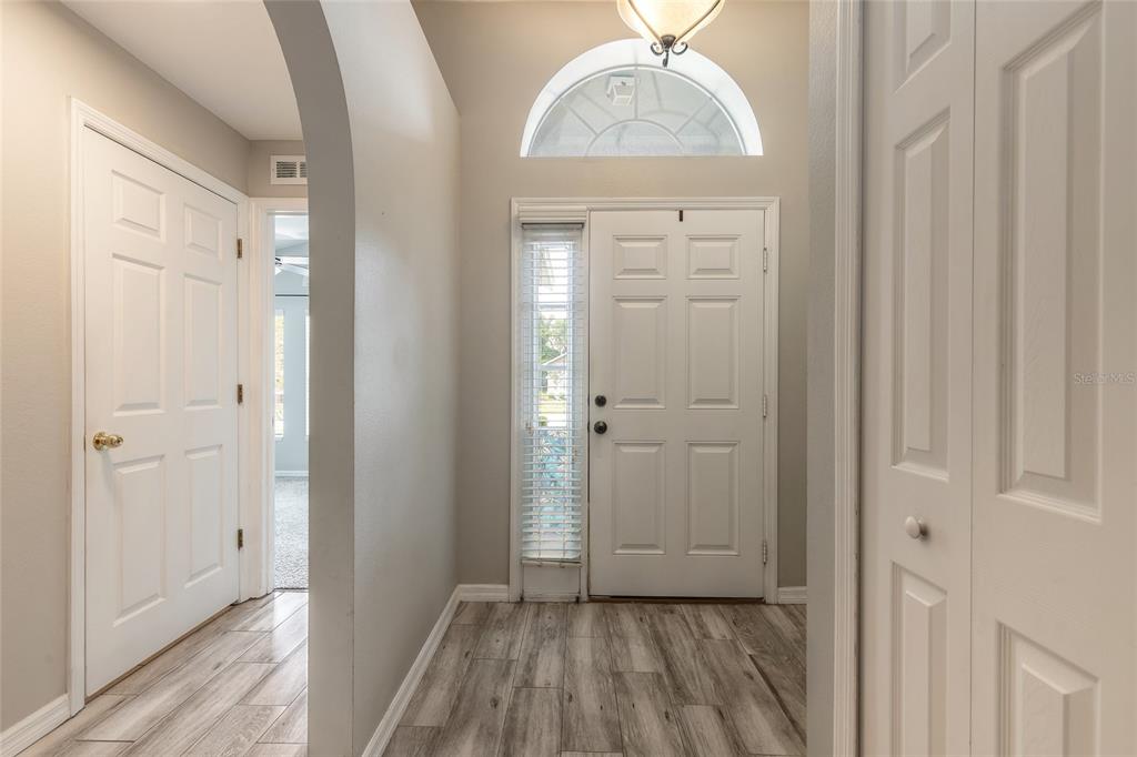 An entryway with light wood-look flooring, a white front door, and an arched doorway — 3873 SUNSET COVE DRIVE, PORT ORANGE, FL