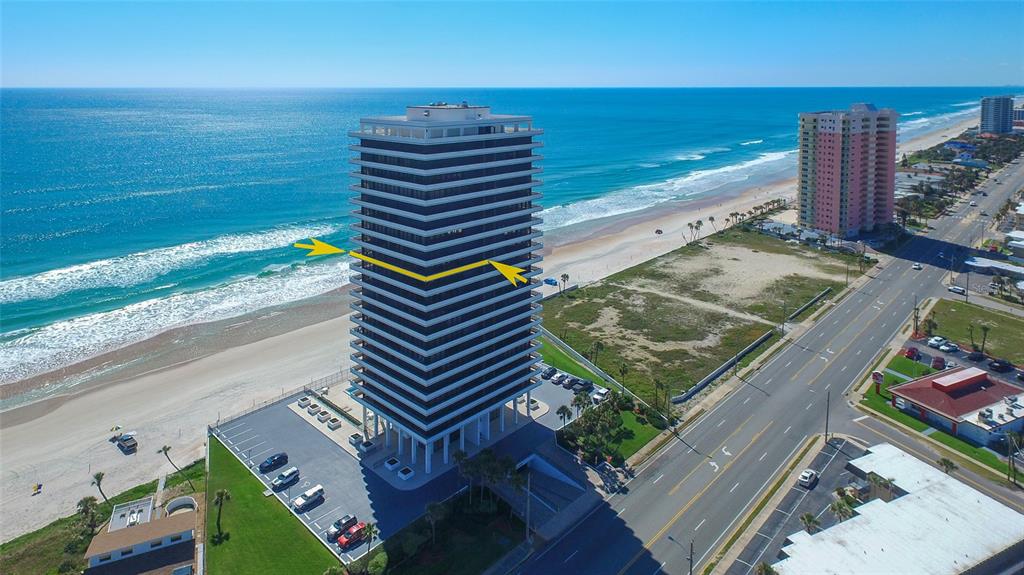 An aerial view of a tall beachfront condominium tower with a yellow arrow pointing toward it — 2200 N ATLANTIC AVENUE UNIT 1201, DAYTONA BEACH, FL