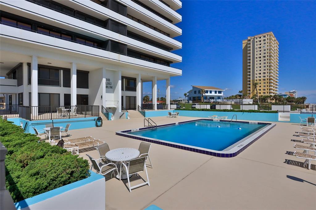 An outdoor swimming pool sits on a concrete deck beside a multi-story residential building — 2200 N ATLANTIC AVENUE UNIT 1201, DAYTONA BEACH, FL