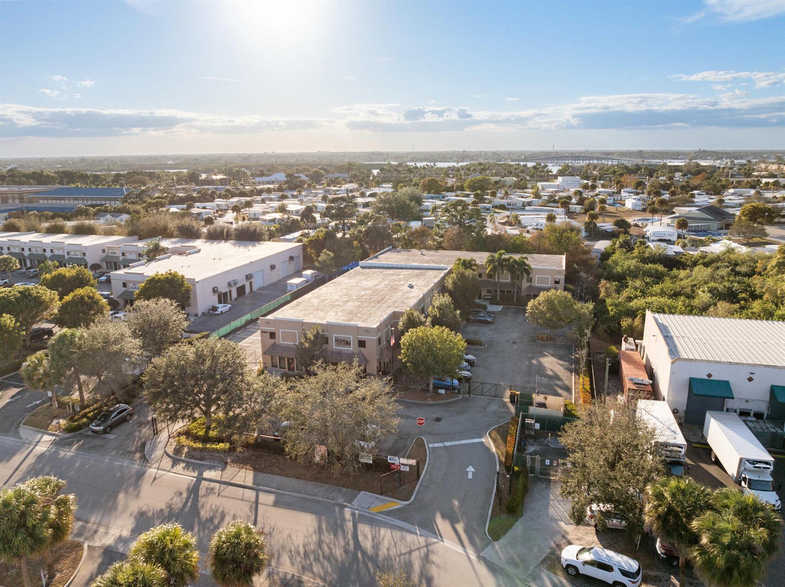 An aerial view shows commercial buildings with parking lots and surrounding trees under a sunny sky — 2580 SE Willoughby Boulevard, Stuart FL 34994, STUART, FL