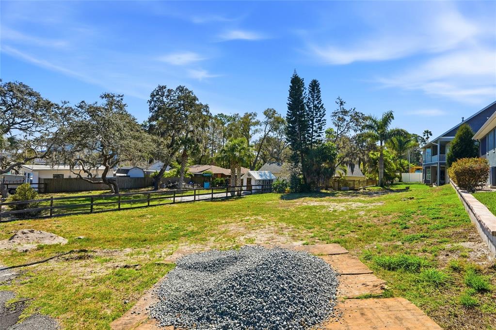 A large, grassy backyard features a pile of gravel, a wooden fence, and mature trees — 1604 BUTLER COURT, TARPON SPRINGS, FL