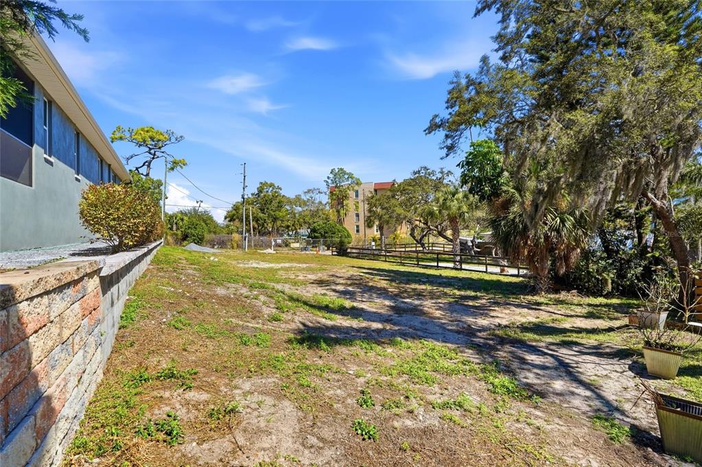 An outdoor view of a vacant, grassy lot next to a house with a retaining wall — 1604 BUTLER COURT, TARPON SPRINGS, FL