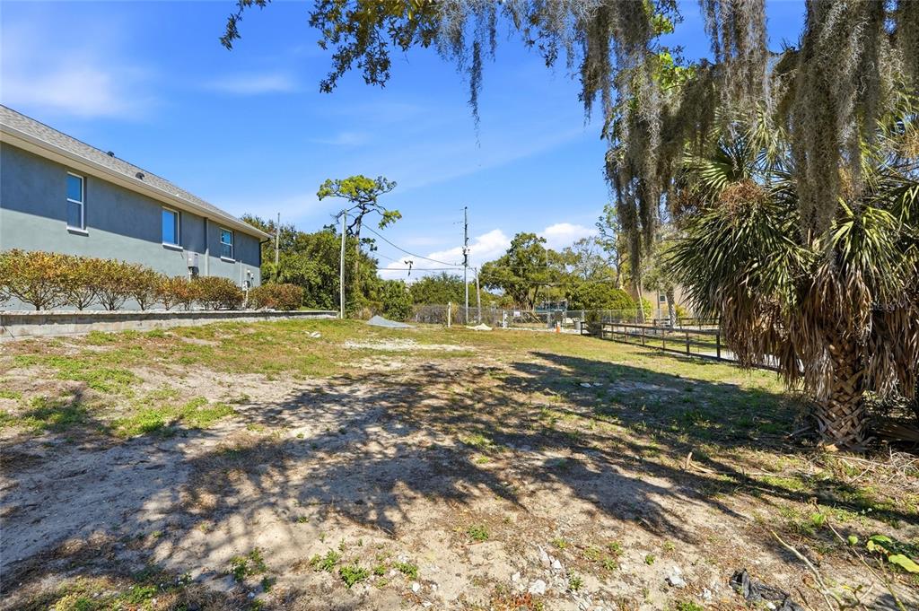 A vacant, sandy residential lot sits next to a gray house with a retaining wall — 1604 BUTLER COURT, TARPON SPRINGS, FL
