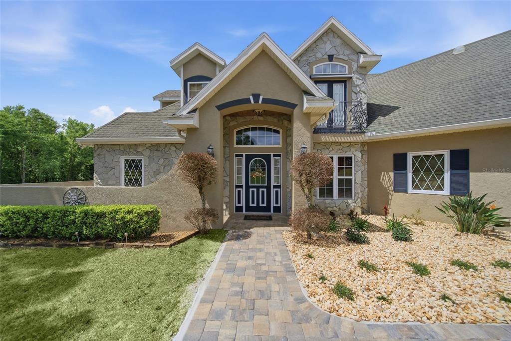 The front exterior of a two-story home features stone accents, a paved walkway, and landscaping — 32640 BLUEBERRY HILL WAY, DADE CITY, FL