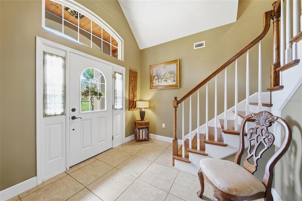 An entryway with tile floors, a white front door, and a staircase with wooden railings — 32640 BLUEBERRY HILL WAY, DADE CITY, FL