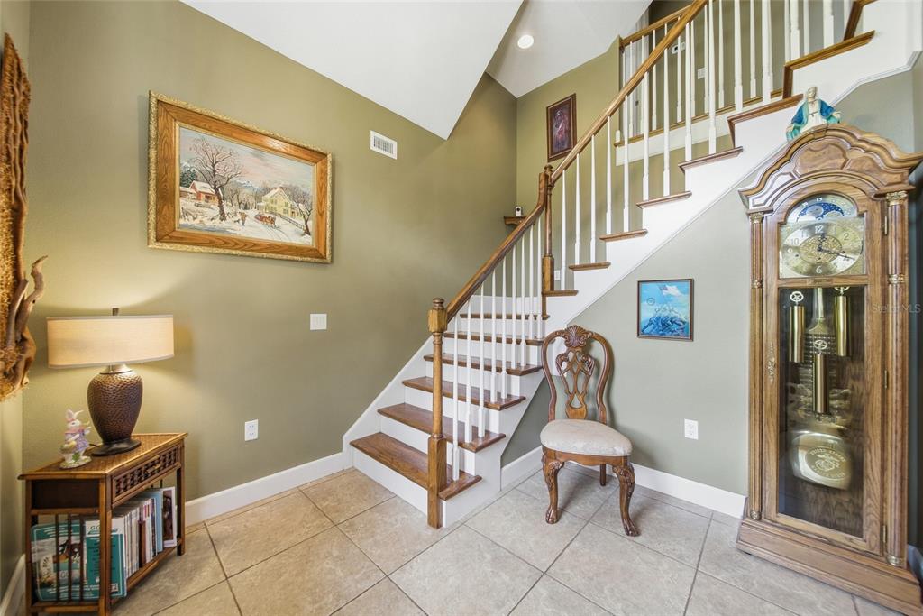 An entryway features a wooden staircase, a grandfather clock, a side table, and tiled flooring — 32640 BLUEBERRY HILL WAY, DADE CITY, FL