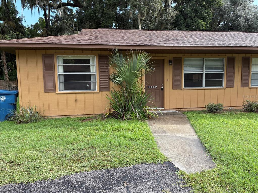 A single-story tan house with brown shutters, a brown door, and a concrete walkway — 20015 SUNCREST DRIVE, BROOKSVILLE, FL