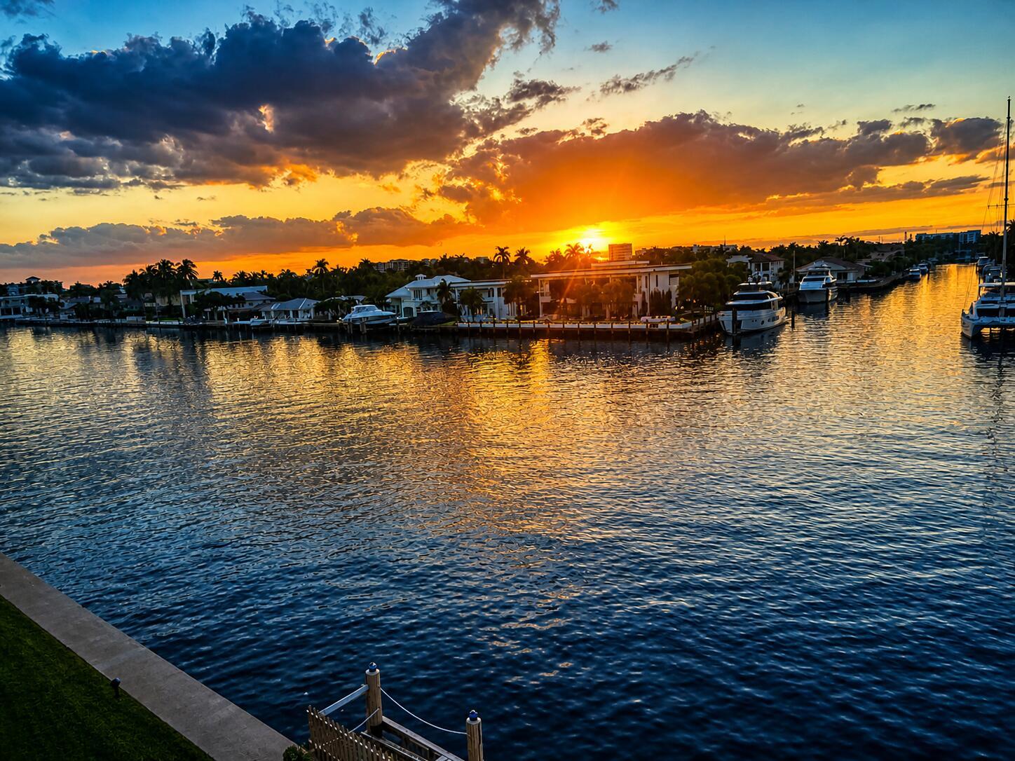 A sunset view over a canal lined with luxury homes, palm trees, and docked yachts — 401 N Riverside Drive # 406, Pompano Beach FL 33062, POMPANO BEACH, FL