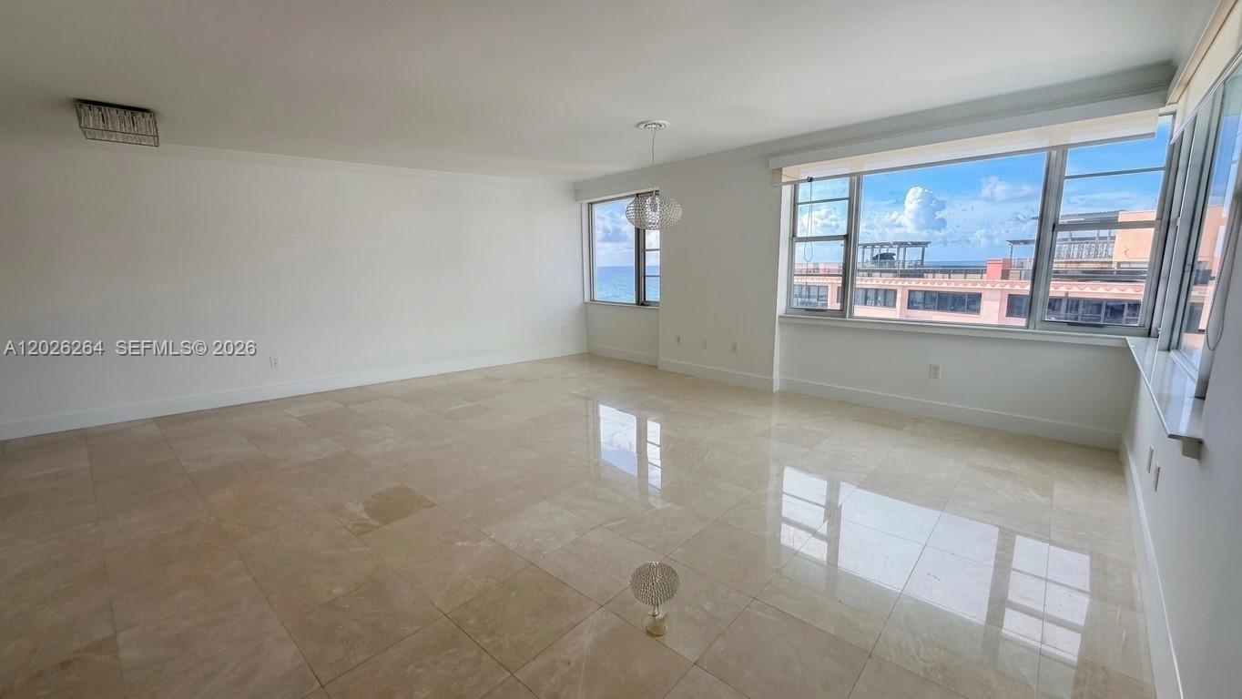An empty room with light-colored tile floors, white walls, and large windows overlooking the ocean — MIAMI BEACH, FL