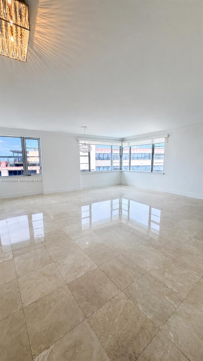 A bright, empty room features polished beige tile flooring and large windows with exterior views — MIAMI BEACH, FL