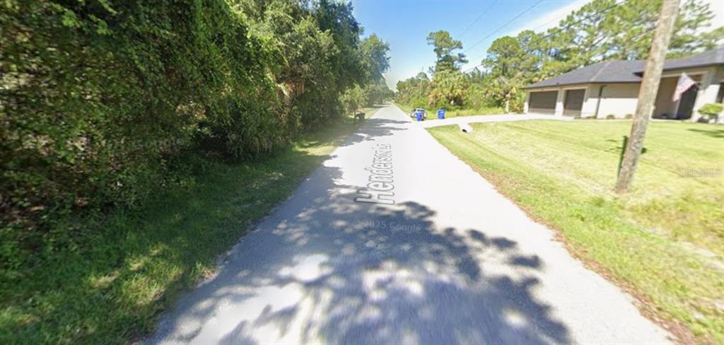 A paved road runs between a wooded area and a house with a lawn — HENDERSON LANE, NORTH PORT, FL