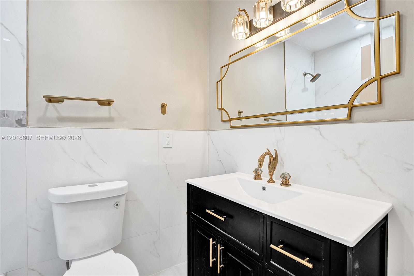 A bathroom features a black vanity, gold fixtures, a decorative mirror, and white marble-look tiles — 3401 NW 7th St, Lauderhill FL 33311, LAUDERHILL, FL