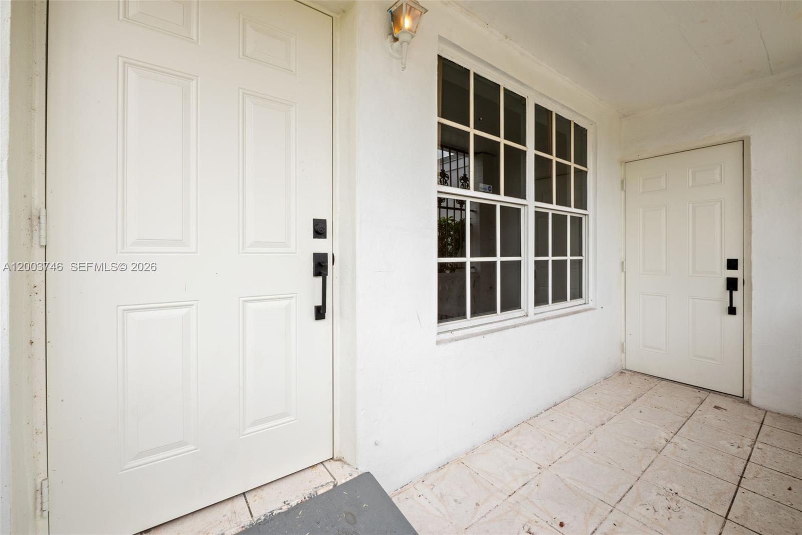 A white exterior entryway features two paneled doors, a grid-patterned window, and tiled flooring — 1130 NW 129th St, North Miami FL 33168, NORTH MIAMI, FL