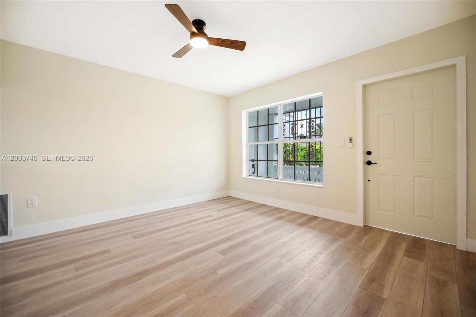 An empty room features light wood-look flooring, a ceiling fan, and a window with security bars — 1130 NW 129th St, North Miami FL 33168, NORTH MIAMI, FL